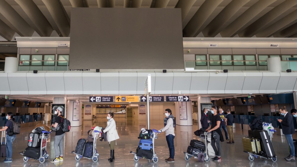 pasajeros en fila en un aeropuerto, con carritos de equipaje