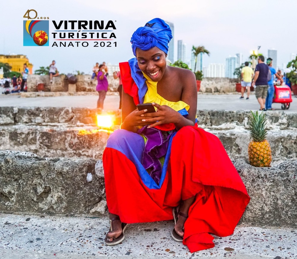 mujer con trajes típicos de Colombia mira un celular, logo de ANATO